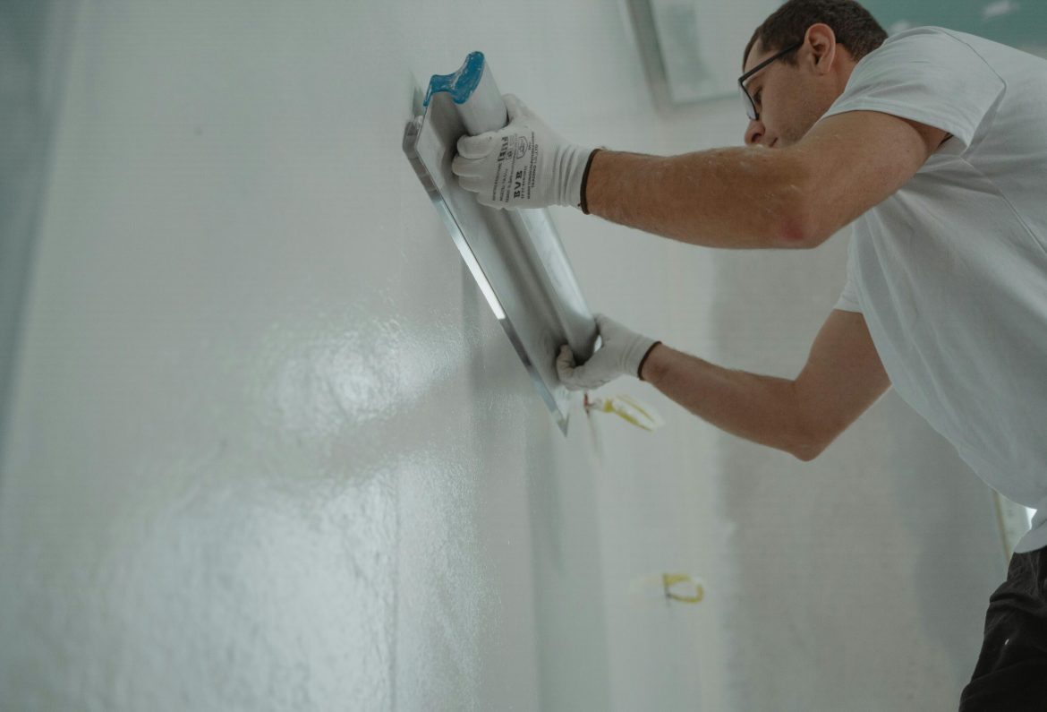 A man works on home renovation, applying plaster to an interior wall for a smooth finish.